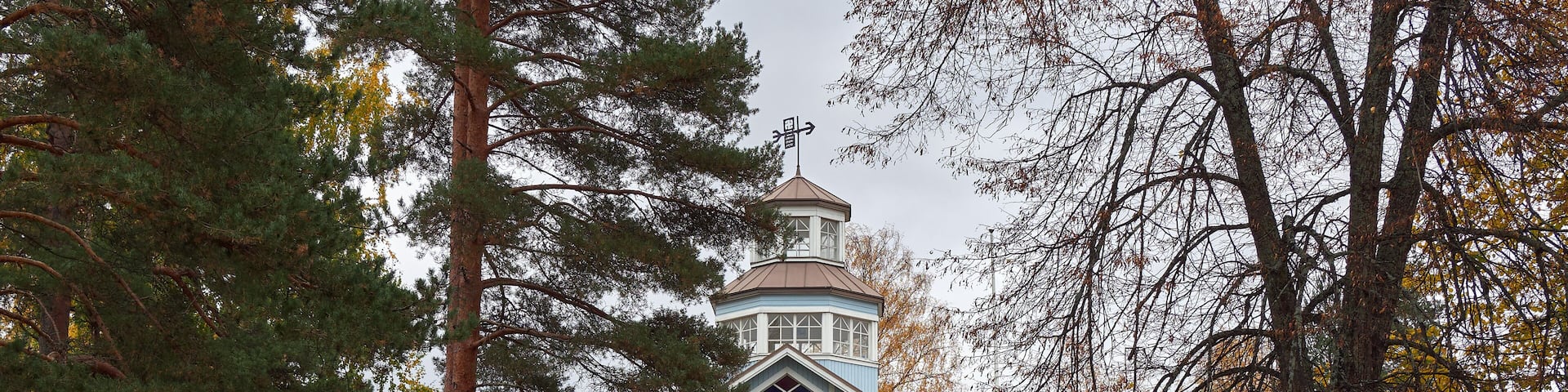 A large blue house with a tower, surrounded by trees and benches.