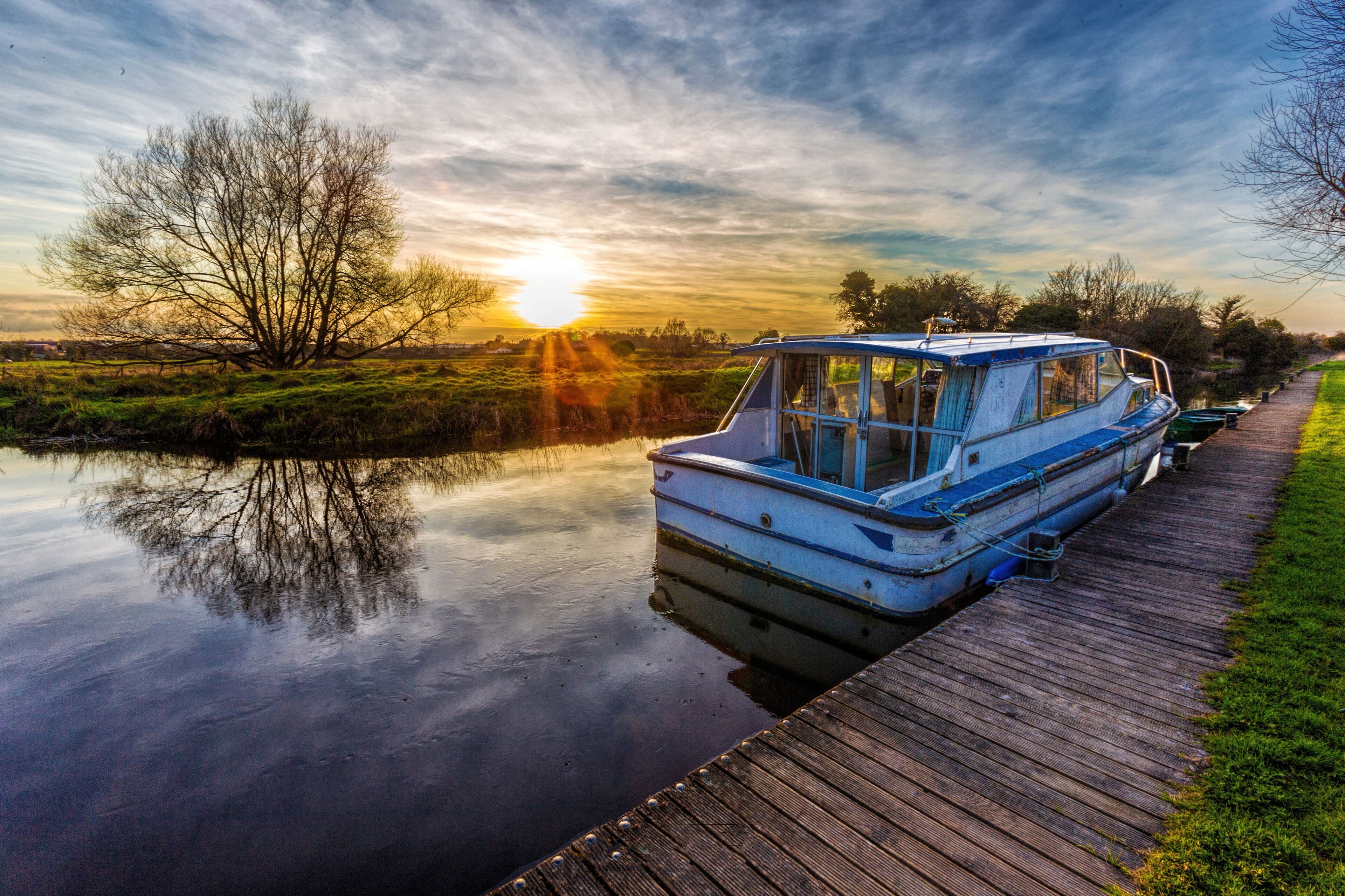 A calm river with a wooden dock, a boat, and a sunset in the background.
