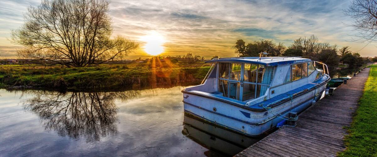 A calm river with a wooden dock, a boat, and a sunset in the background.