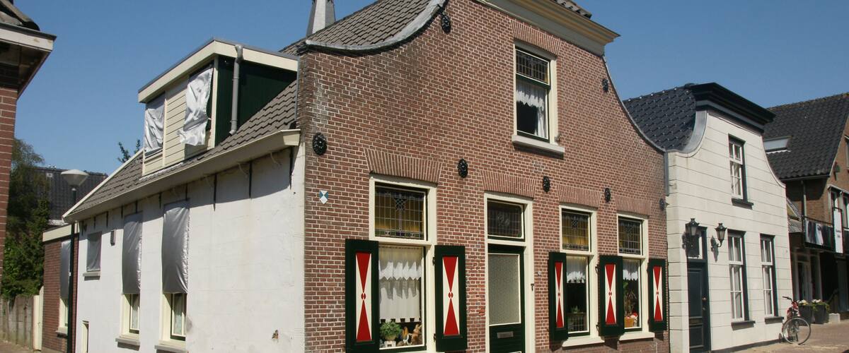 A brick building with white walls and green shutters, a bicycle parked outside, and a clear blue sky.