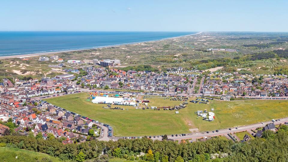 An aerial view of a coastal town with a large open field, residential areas, and a beach.