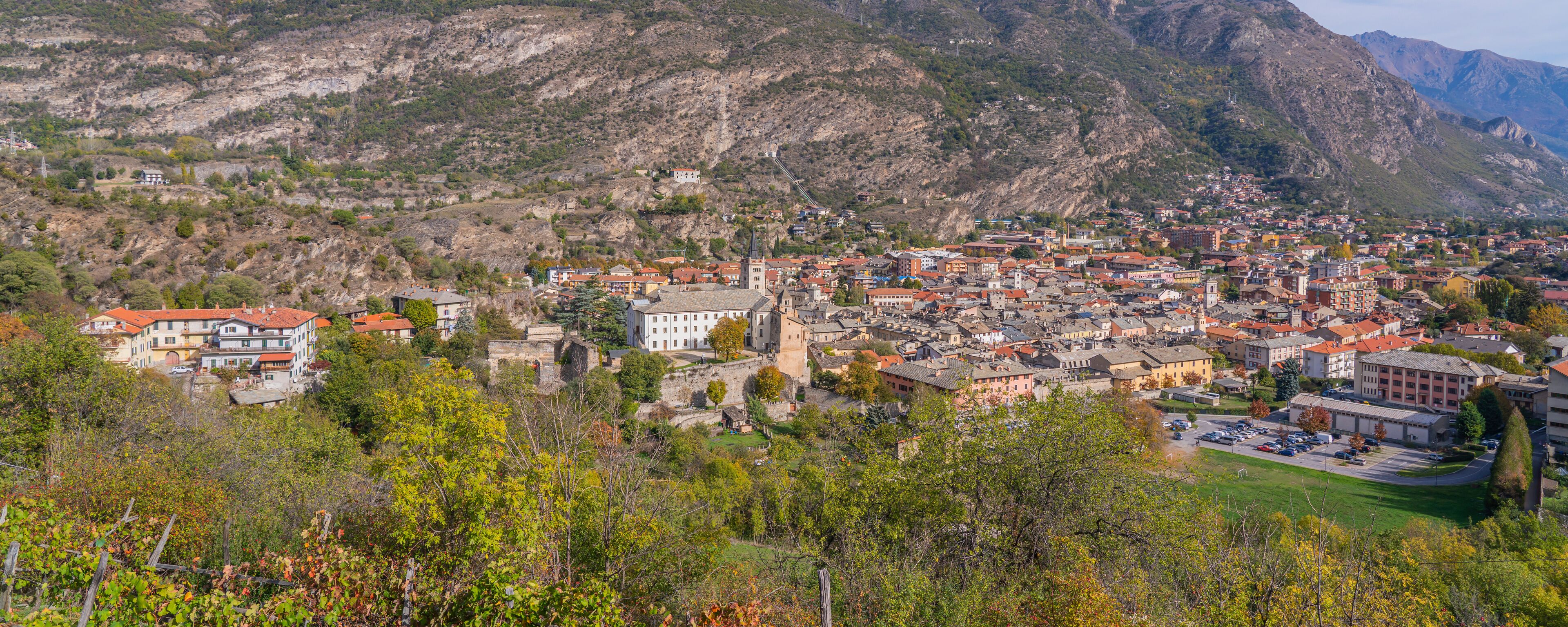 A town nestled in a valley with mountains in the background, featuring historic buildings and a prominent church tower.