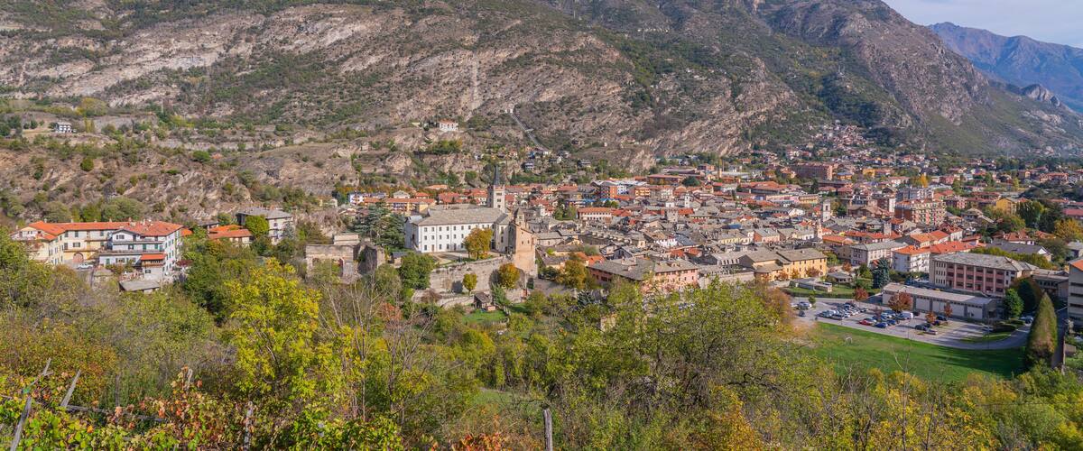 A town nestled in a valley with mountains in the background, featuring historic buildings and a prominent church tower.