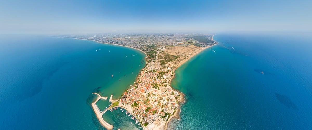 An aerial view of a coastal city with a bay, clear blue waters, and a densely built urban area.