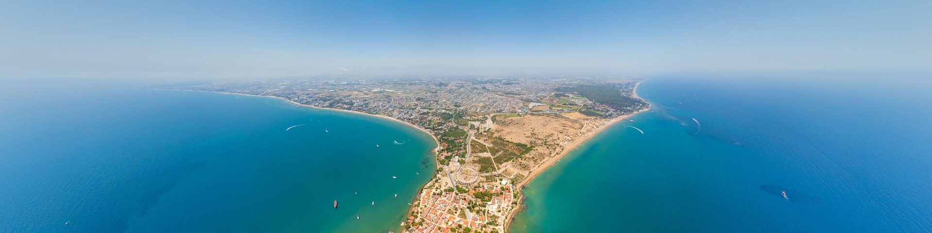 An aerial view of a coastal city with a bay, clear blue waters, and a densely built urban area.
