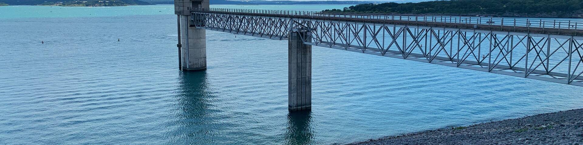 A bridge over calm water with a rocky shoreline and a clear sky.