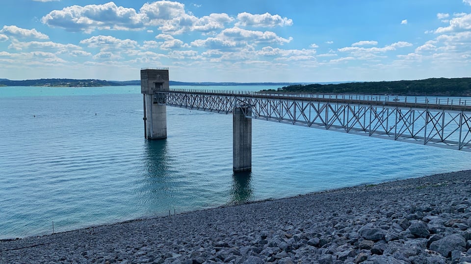 A bridge over calm water with a rocky shoreline and a clear sky.