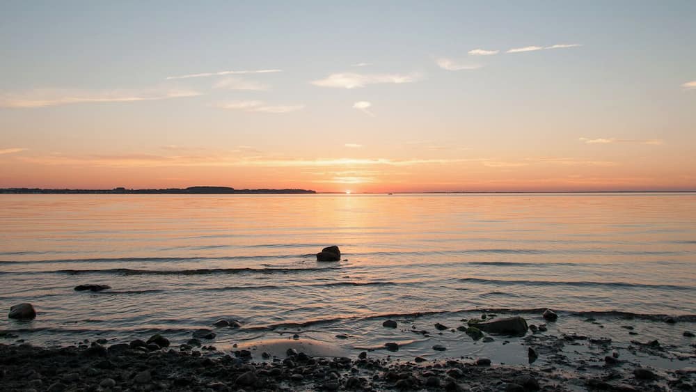 A sunset over a calm sea with rocks in the foreground.