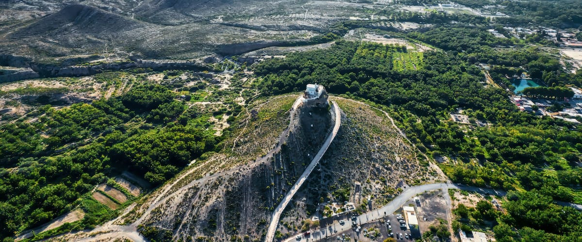 A mountainous landscape with a winding road and a prominent white building on a hill.