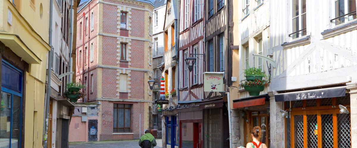 A narrow cobblestone street lined with historic buildings, a person walking, and a shop with a sign reading "Crépierie".