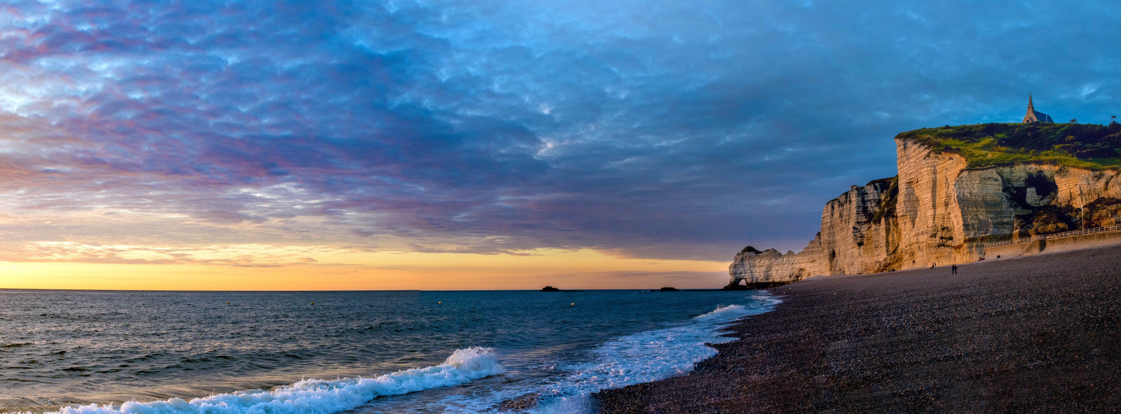 Un paysage côtier avec une falaise, une plage et une île au loin.
