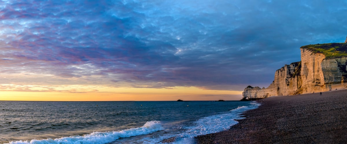 Un paysage côtier avec une falaise, une plage et une île au loin.
