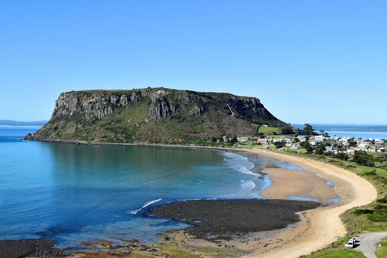 Un paisaje costero con un acantilado destacado, una playa de arena y un pequeño asentamiento.