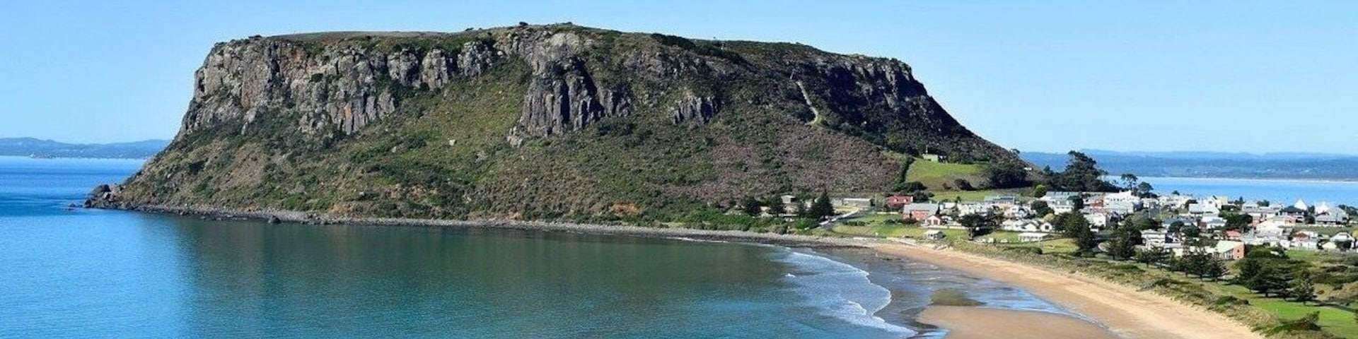 Un paisaje costero con un acantilado destacado, una playa de arena y un pequeño asentamiento.