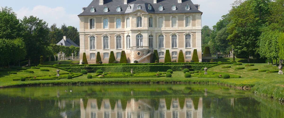 A large, historic building with a symmetrical facade, a central staircase, and a surrounding formal garden with a pond.