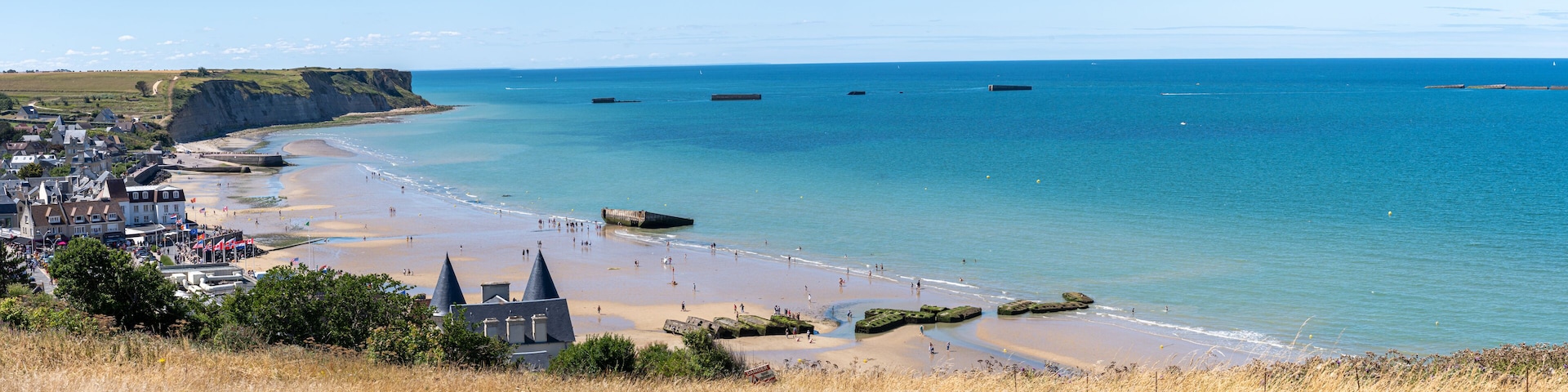 Un pueblo costero con una playa, acantilados y un mar azul cristalino.