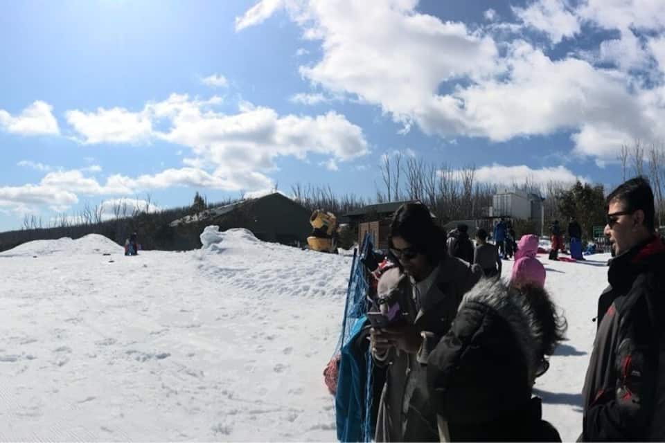 Una pista da sci innevata con una recinzione, edifici e cielo sereno.
