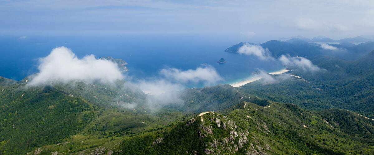 A mountainous landscape with lush greenery, a winding road, and a distant view of the ocean.