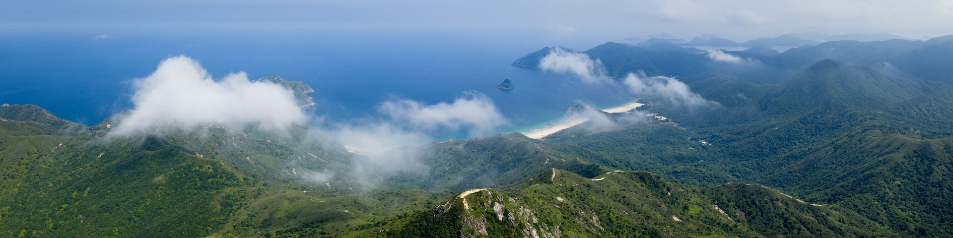 A mountainous landscape with lush greenery, a winding road, and a distant view of the ocean.