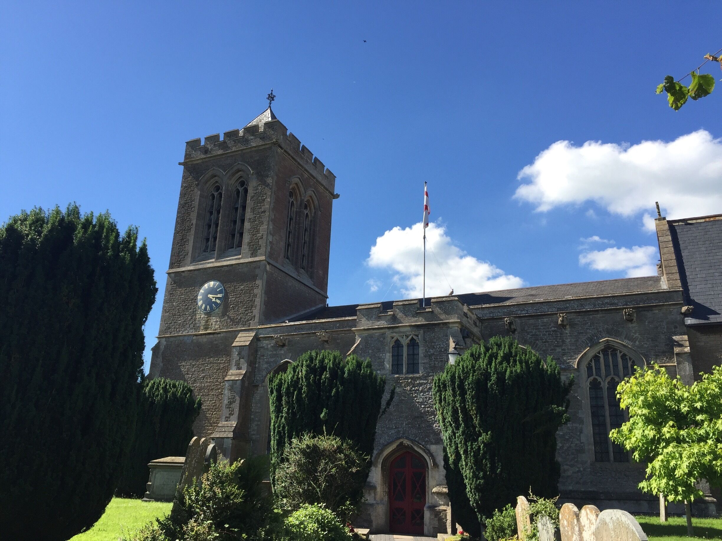 A church with a clock tower, a red door, and a flagpole.