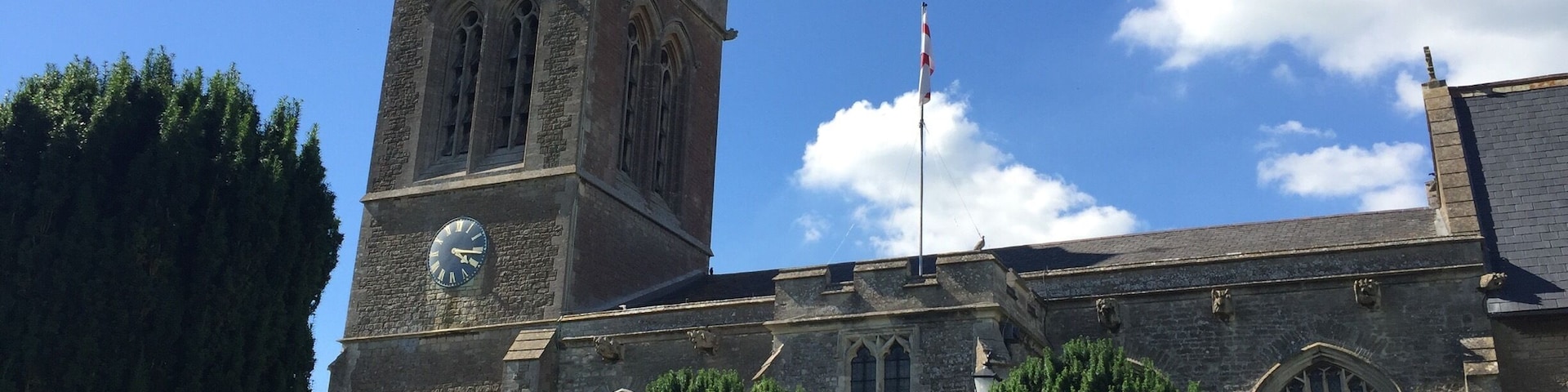 A church with a clock tower, a red door, and a flagpole.