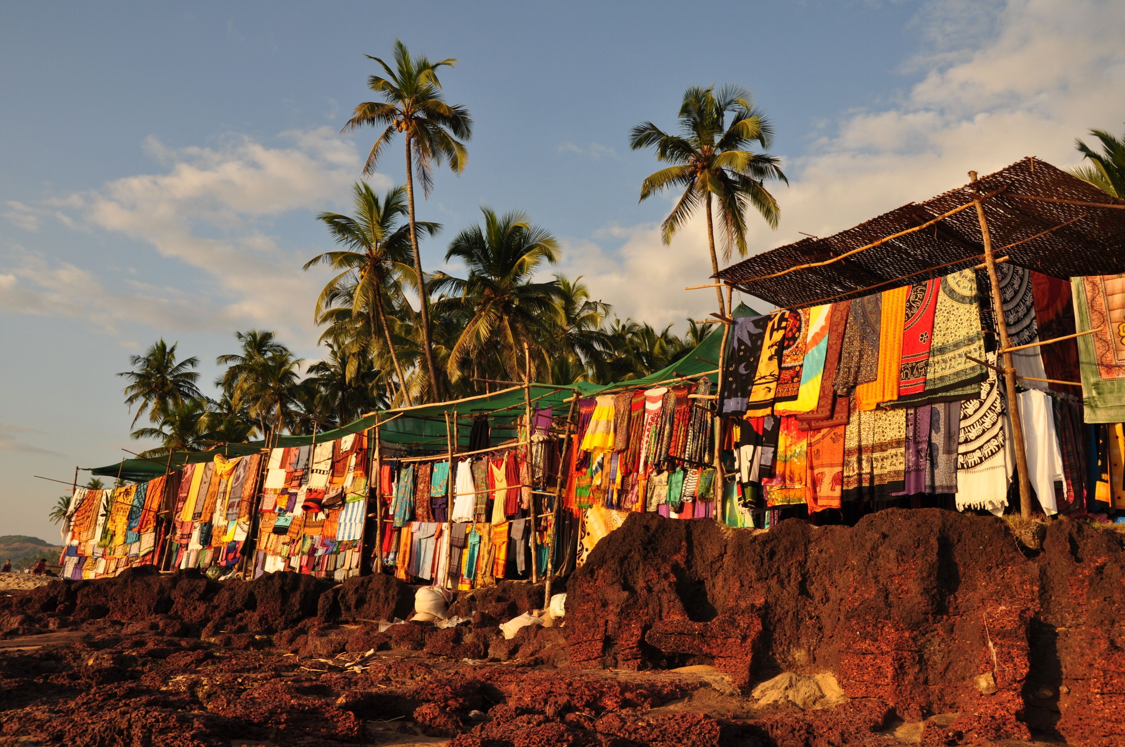 A beach with colorful fabrics hanging on a structure, palm trees, and a clear sky.