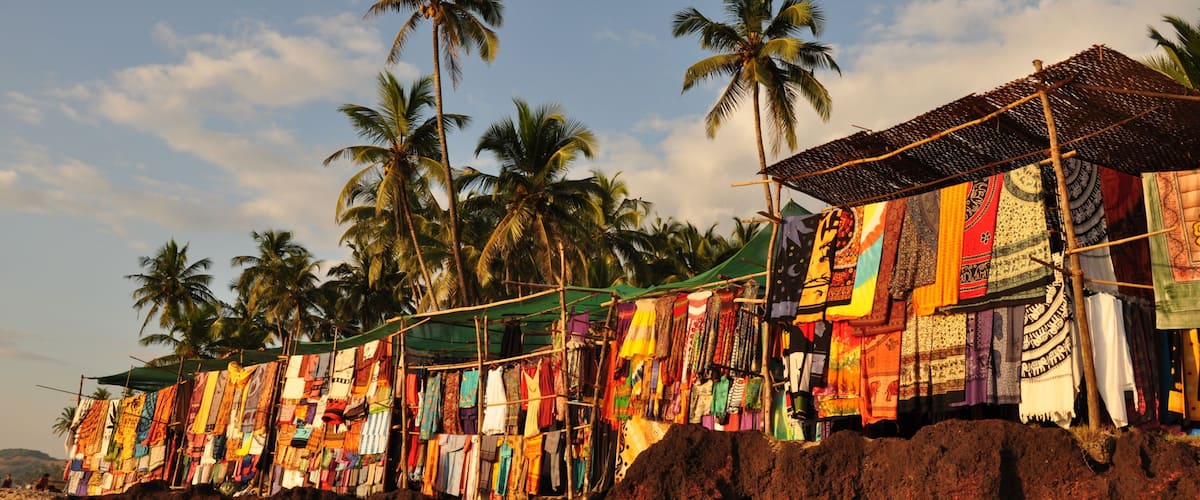 A beach with colorful fabrics hanging on a structure, palm trees, and a clear sky.