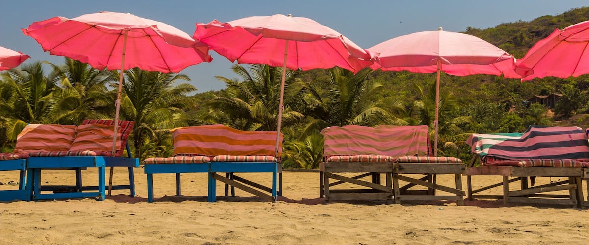 Una playa con varios sombrillas rosadas y sillas de descanso a rayas.