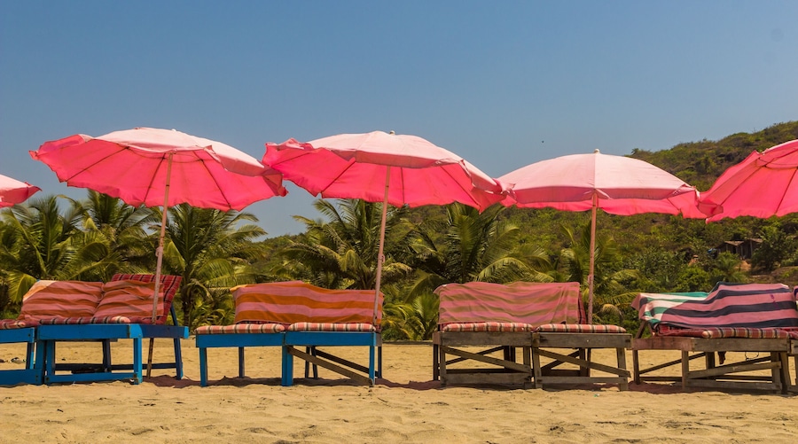 Une plage avec de nombreux parasols roses et des chaises longues à rayures.