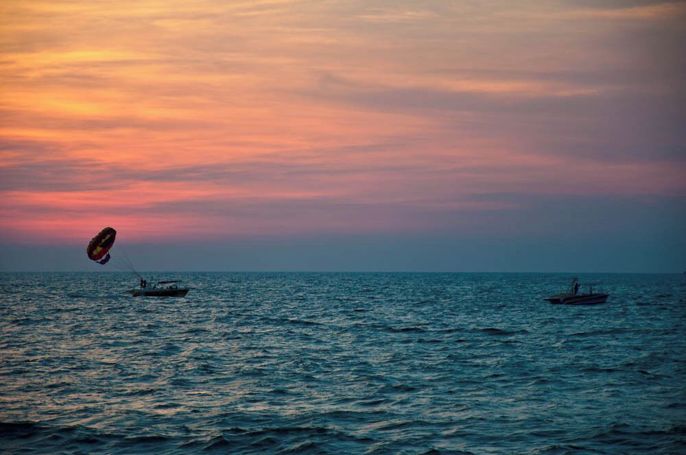 A sunset over the ocean with two boats and a kite.