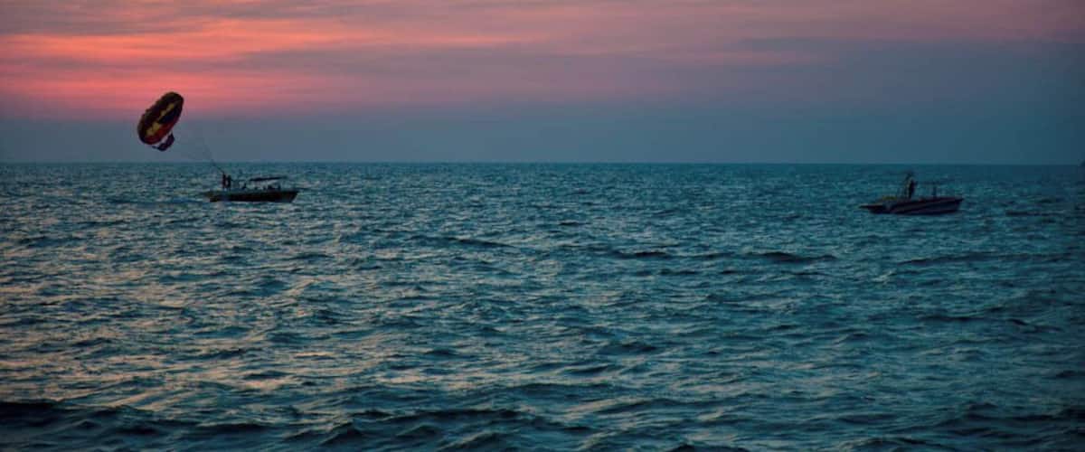 A sunset over the ocean with two boats and a kite.