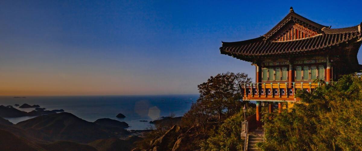 A traditional Chinese pagoda overlooking a coastal landscape with mountains and the sea.