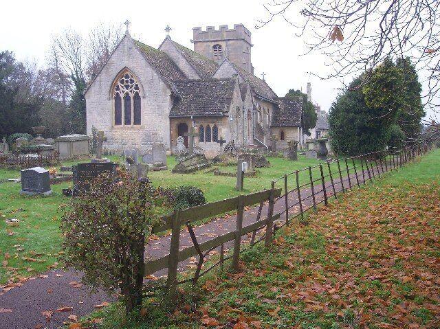 A church with a stone facade and a tall steeple, surrounded by a cemetery with headstones and a wooden fence.