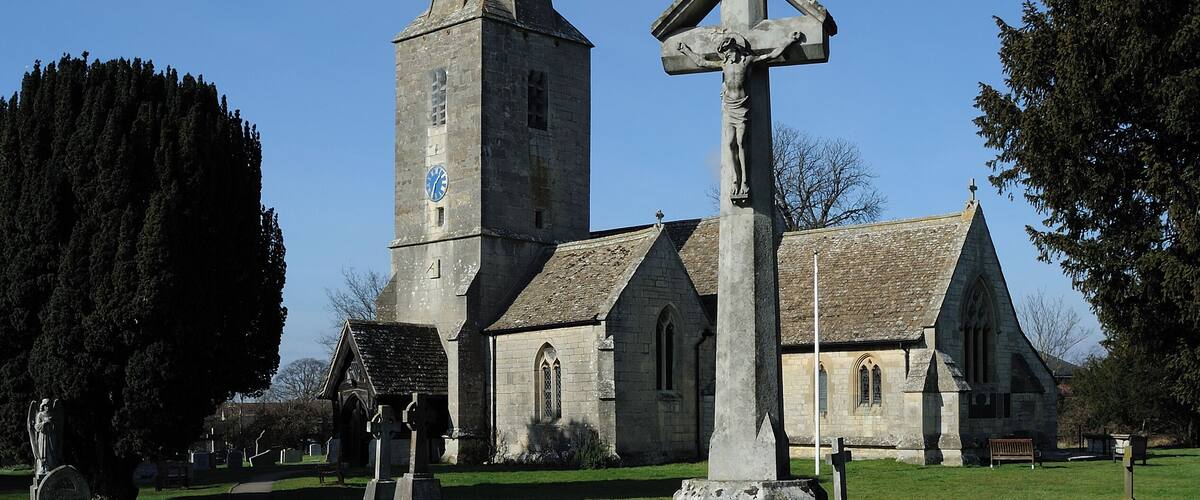 A church with a tall steeple and a cross monument in the foreground.