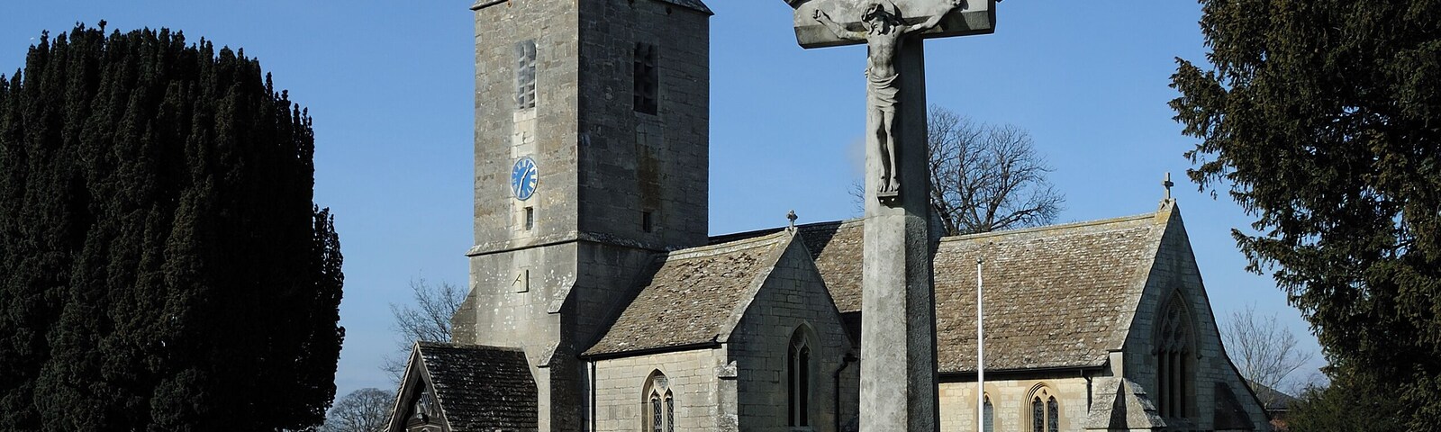 A church with a tall steeple and a cross monument in the foreground.