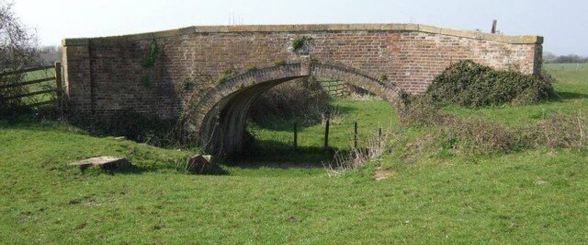 A brick arch bridge in a grassy field.
