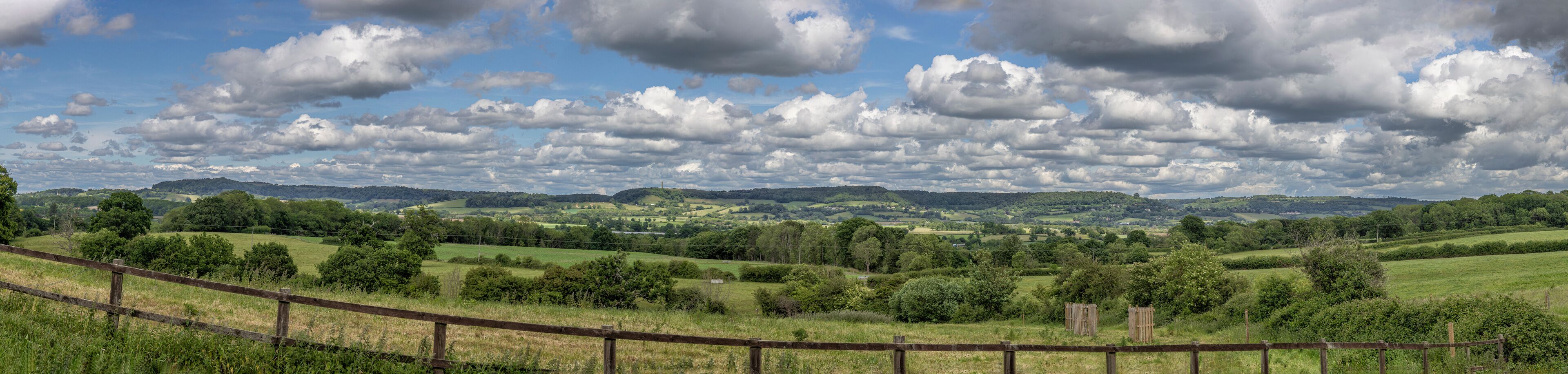 A rural landscape with rolling hills, a wooden fence, and a cloudy sky.