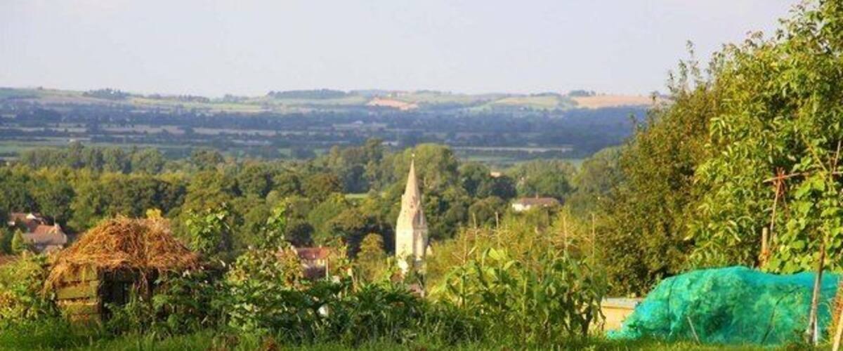 A rural landscape with a church steeple, a haystack, and a green field.