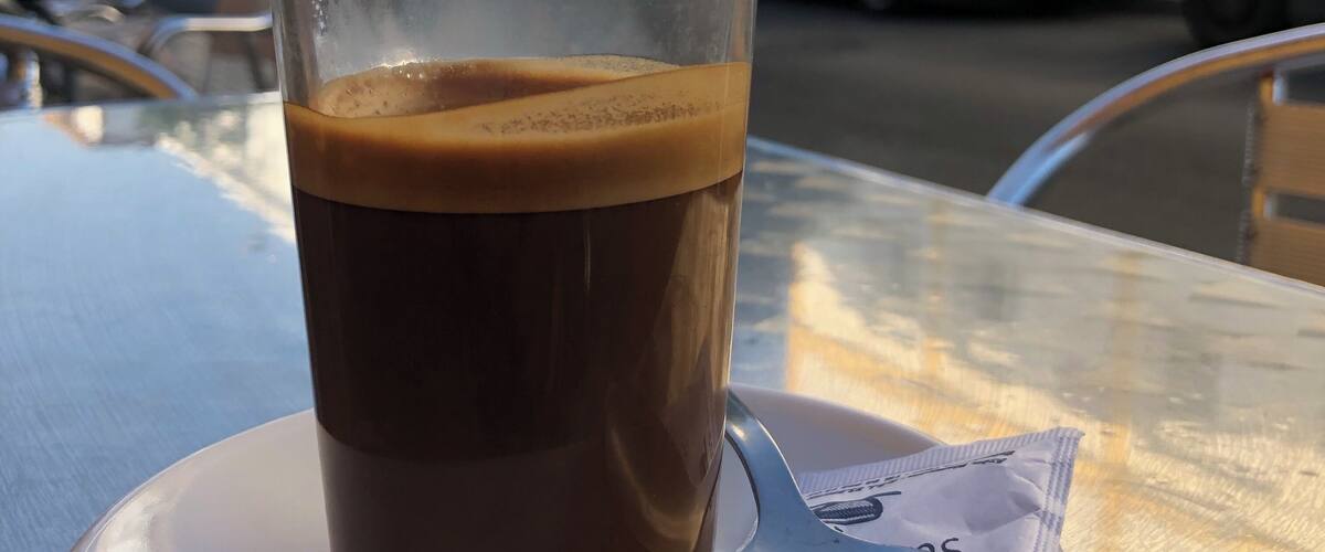 A glass of iced coffee on a table with a spoon and a napkin.