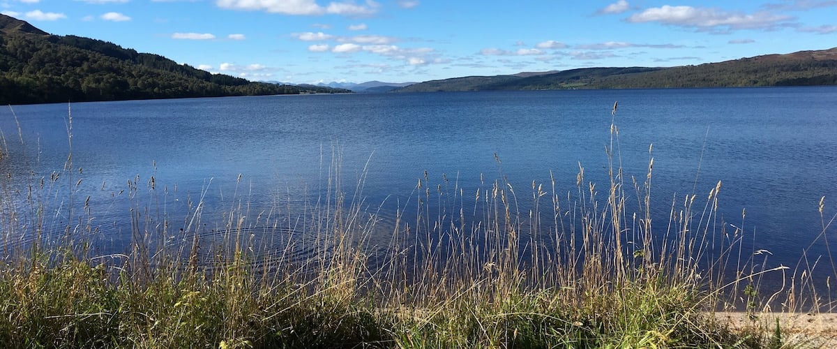 A calm lake surrounded by hills and sparse vegetation.