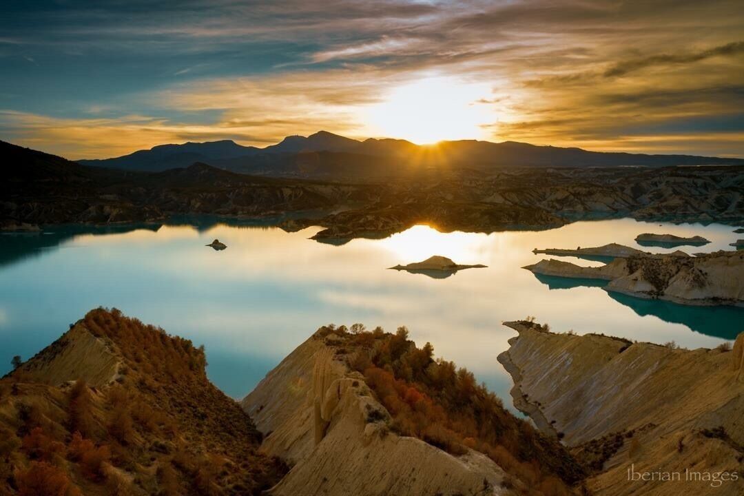 A mountainous landscape with a lake reflecting the sunset.