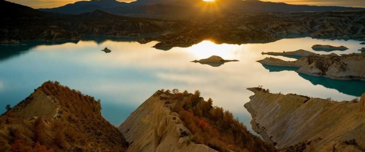 A mountainous landscape with a lake reflecting the sunset.