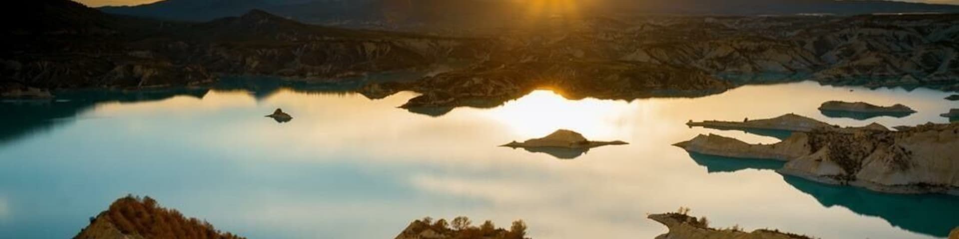 A mountainous landscape with a lake reflecting the sunset.