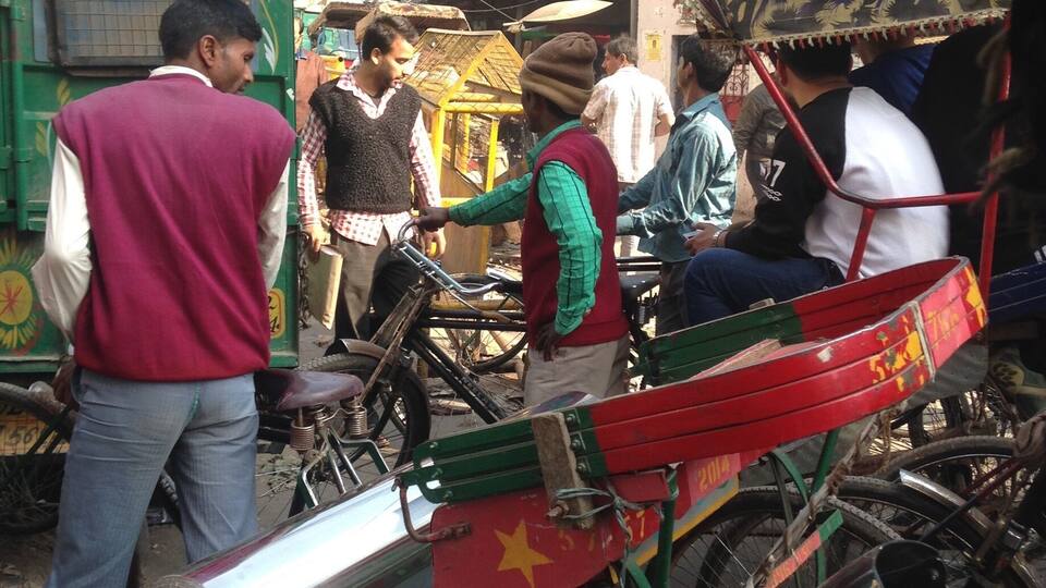 A street scene with a rickshaw, bicycles, and a green truck.