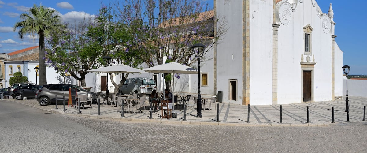 A white church with a clock tower, outdoor seating, and palm trees.