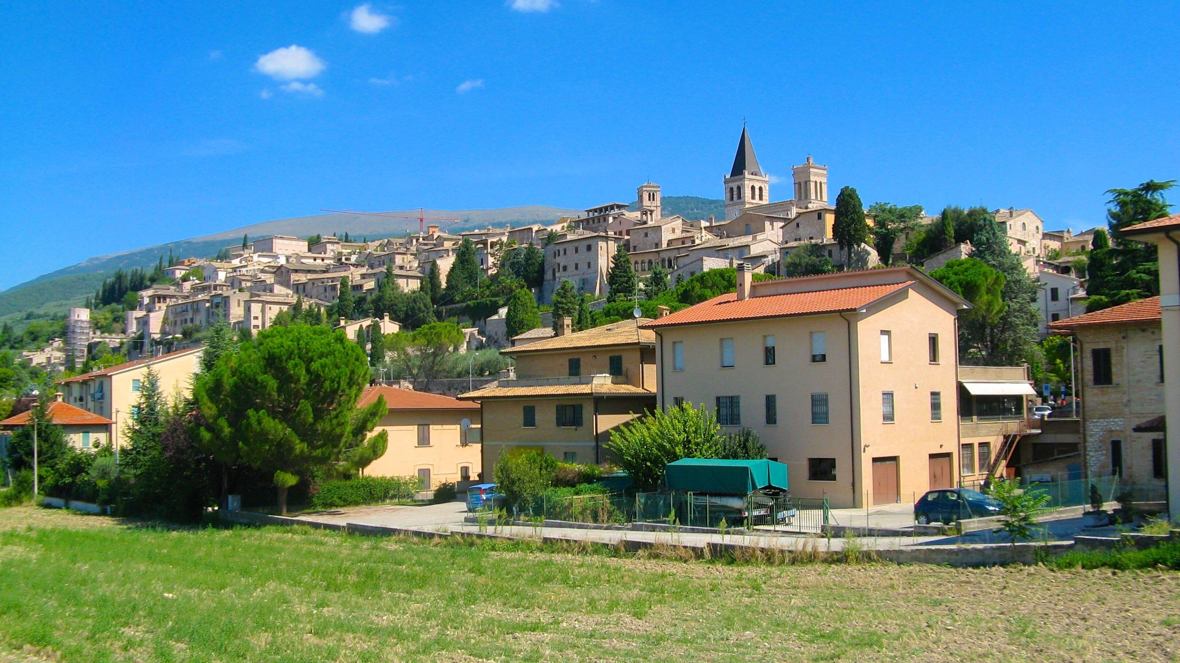 A hillside town with historic buildings, a prominent church with a bell tower, and a clear blue sky.