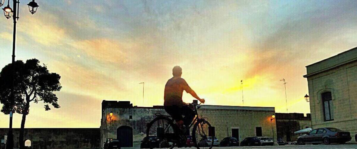 A person riding a bicycle on a cobblestone street during sunset.