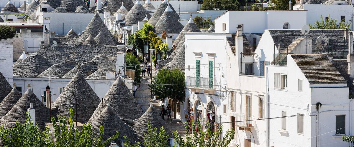 A village with white buildings and conical roofs, surrounded by trees and a hilly landscape.