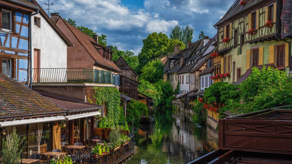 A narrow canal flanked by traditional half-timbered buildings with balconies and flower boxes.
