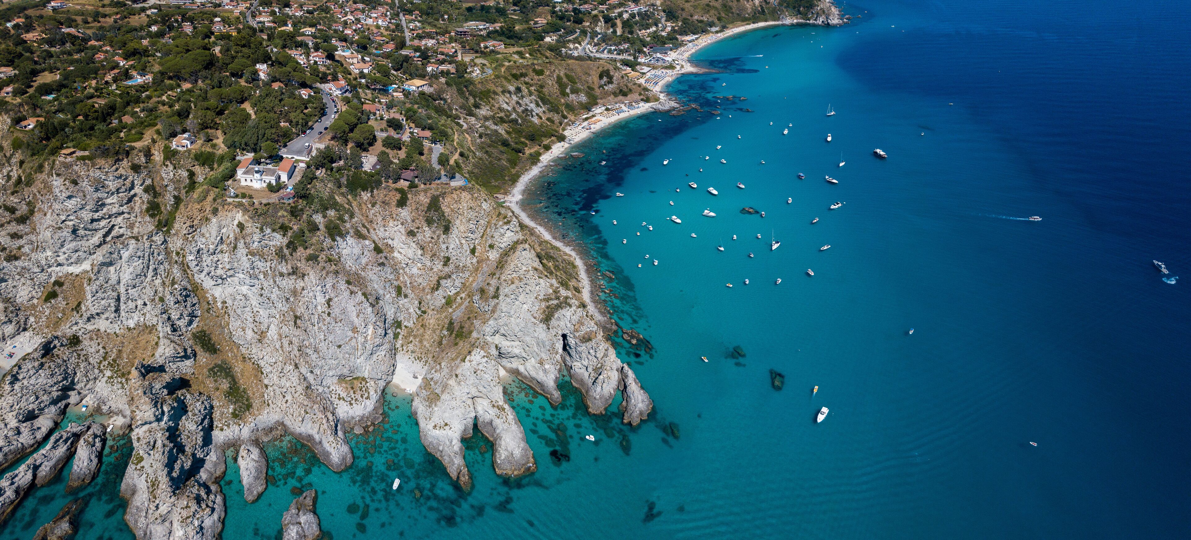 A coastal town with rocky cliffs, clear turquoise waters, and numerous boats.